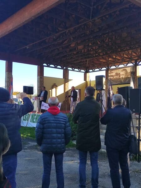 Људи слушају говорнике на бини под надстрешницом