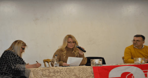 Троје људи за столом, жена говори у микрофон
