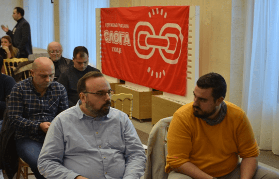 Учесници седе на скупу испред црвеног банера Слога